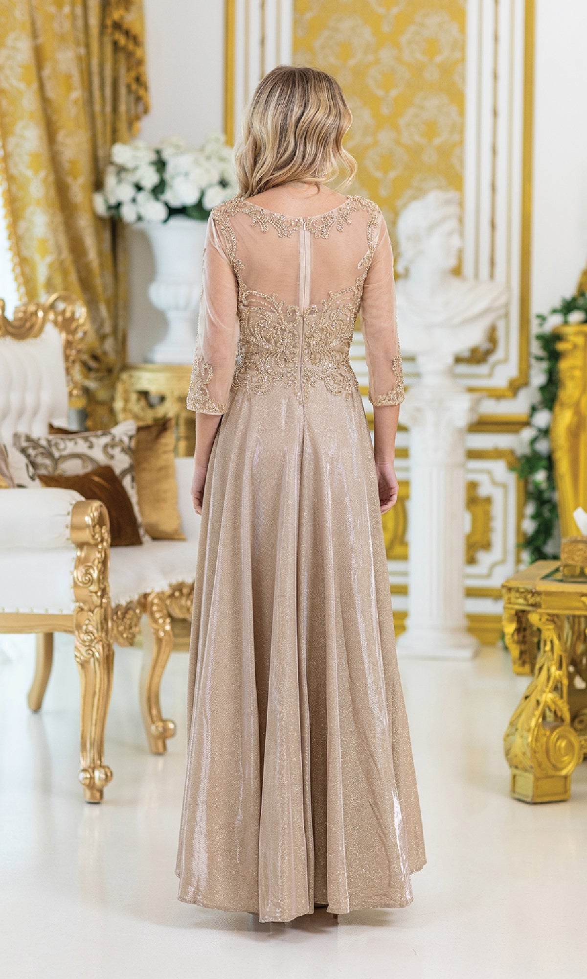 A woman wearing the Lace-Sleeve Long Formal Dress: Dancing Queen 4498, featuring a gold lace bodice, sheer sleeves, and intricate embroidery, stands in an ornate gold room, viewed from the back.